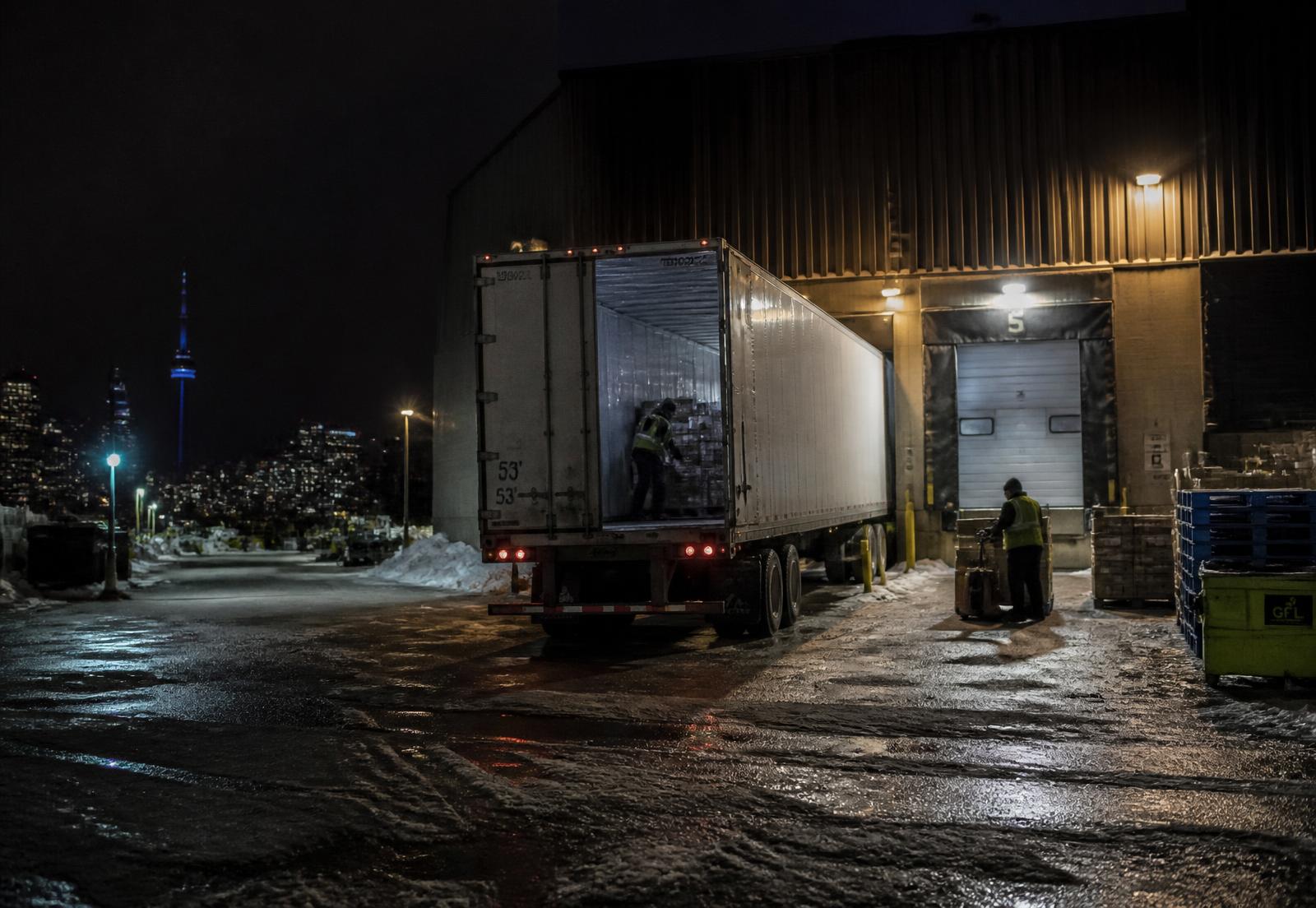 Loading dock at night with roll-up doors open and pallets staged